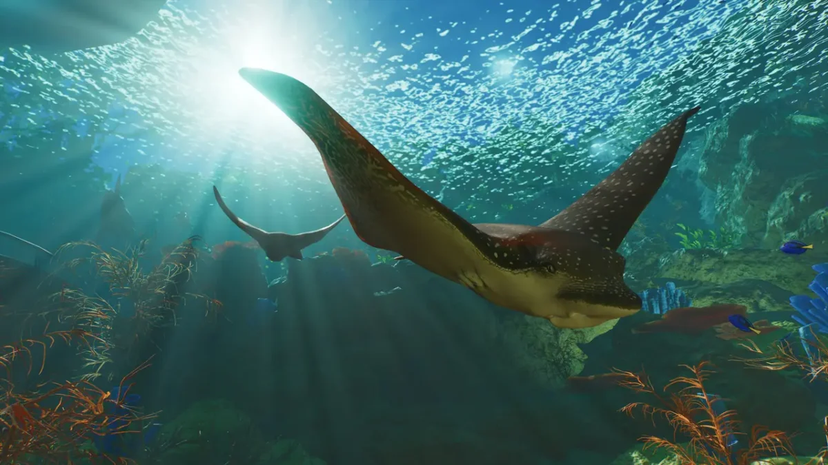 An eagle ray gliding through sunlit water in a Planet Zoo 2 aquarium, with a shoal of fish overhead