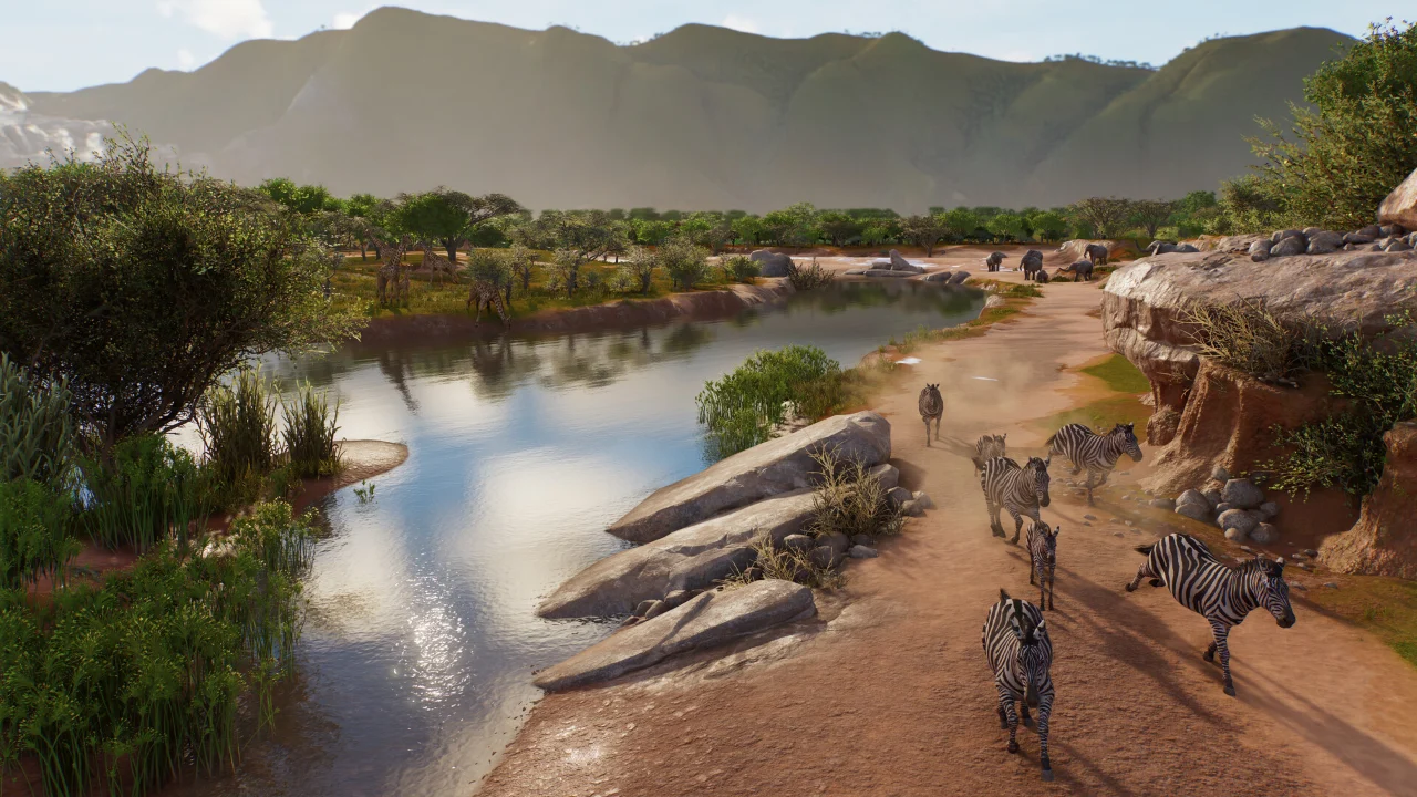 A herd of zebras walking along a river path in a Planet Zoo 2 habitat